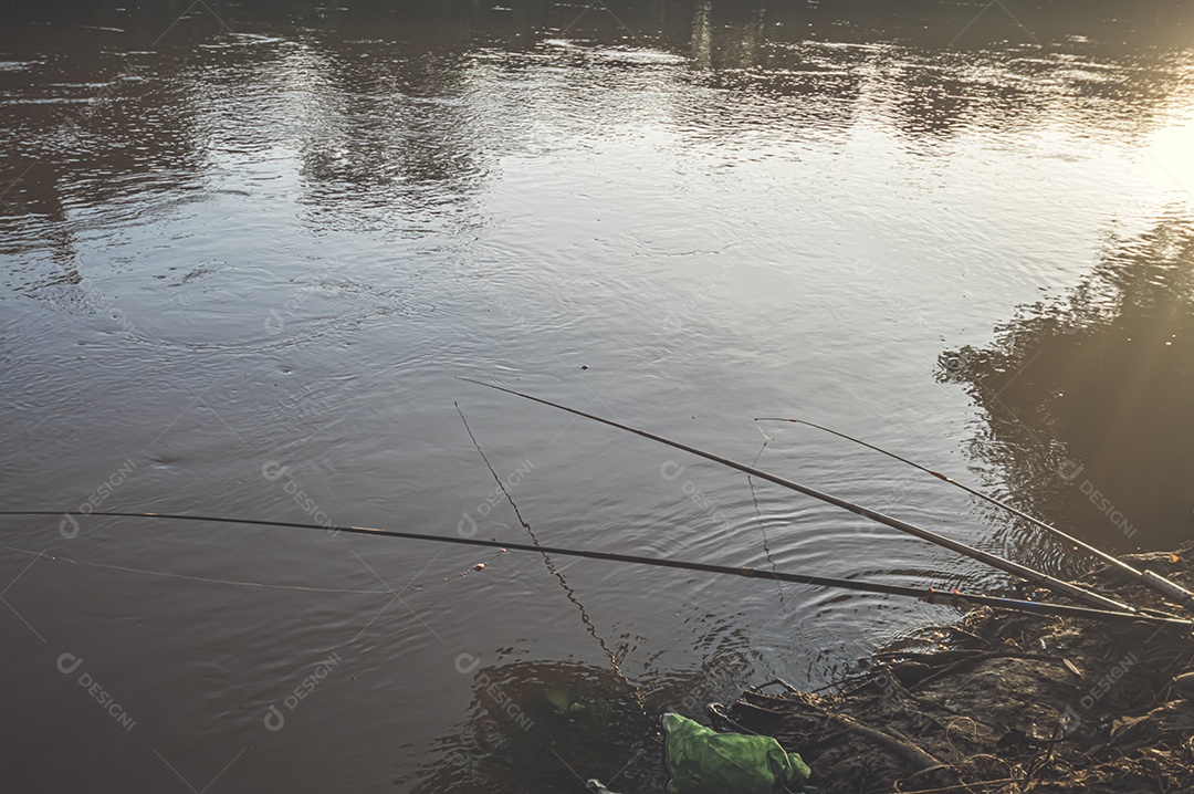 Varas de pesca deixadas por pescadores na beira de um rio no final da tarde, hora de ouro, conceito de pesca.