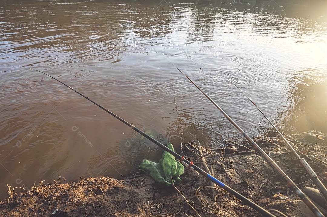 Varas de pesca deixadas por pescadores na beira de um rio no final da tarde, hora de ouro, conceito de pesca.