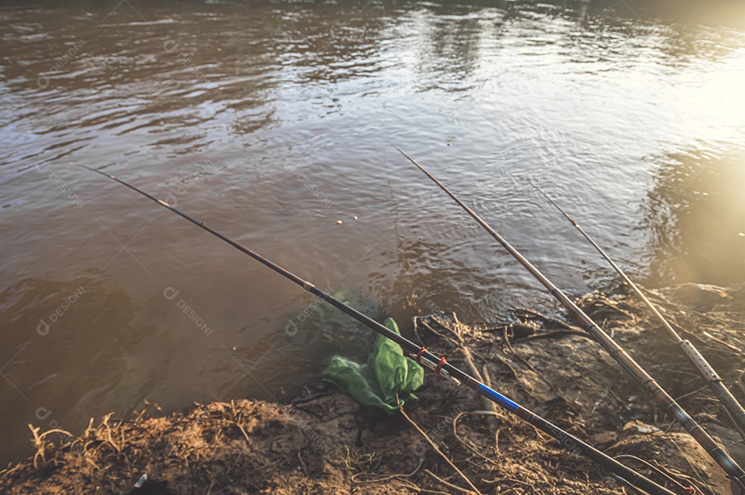 Varas de pesca deixadas por pescadores na beira de um rio no final da tarde, hora de ouro, conceito de pesca.