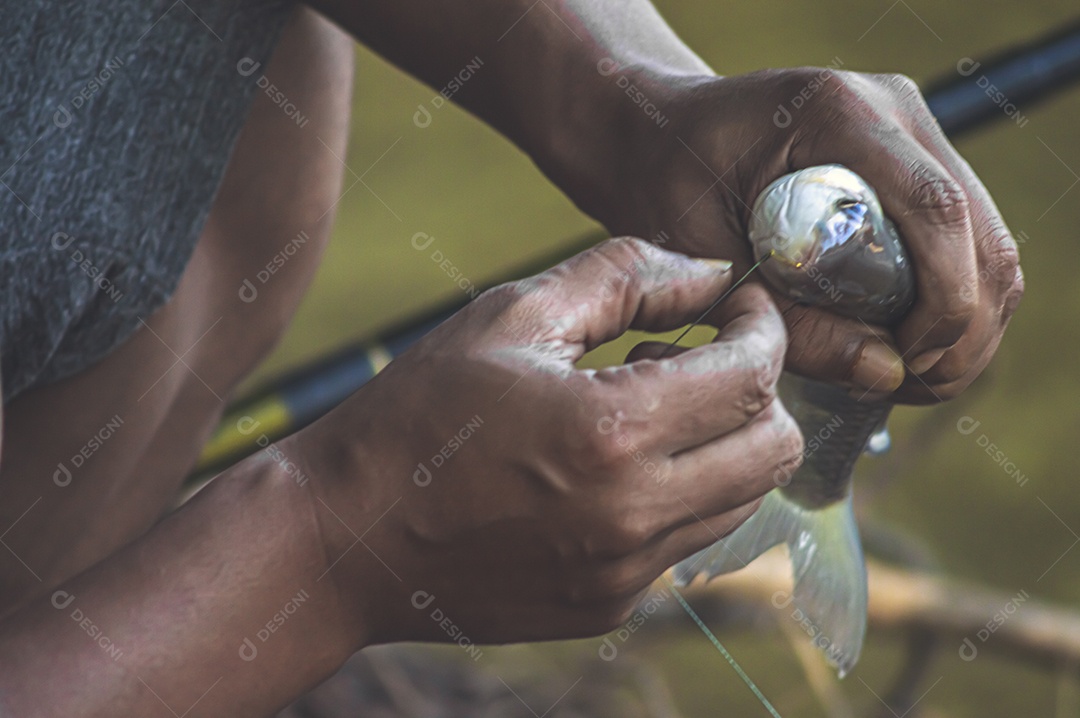 Homem tirando o anzol da boca de um peixe que acabou de pescar, conceito de pesca.