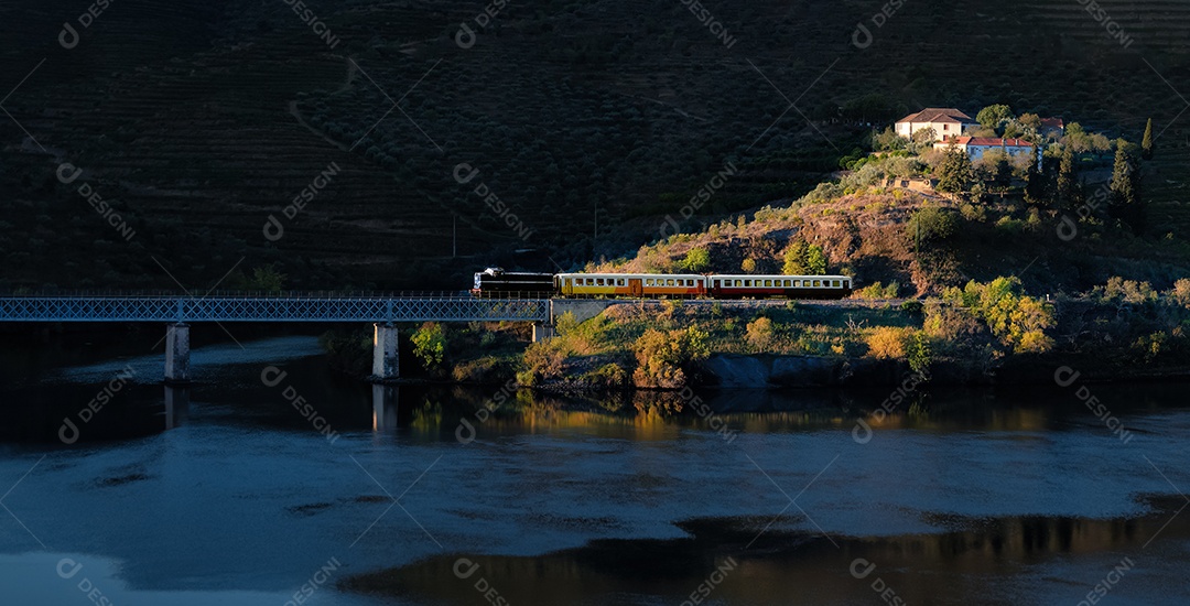 Comboio turístico no vale do Douro, passando na ponte de ferro e iluminado pelos raios do sol da manhã