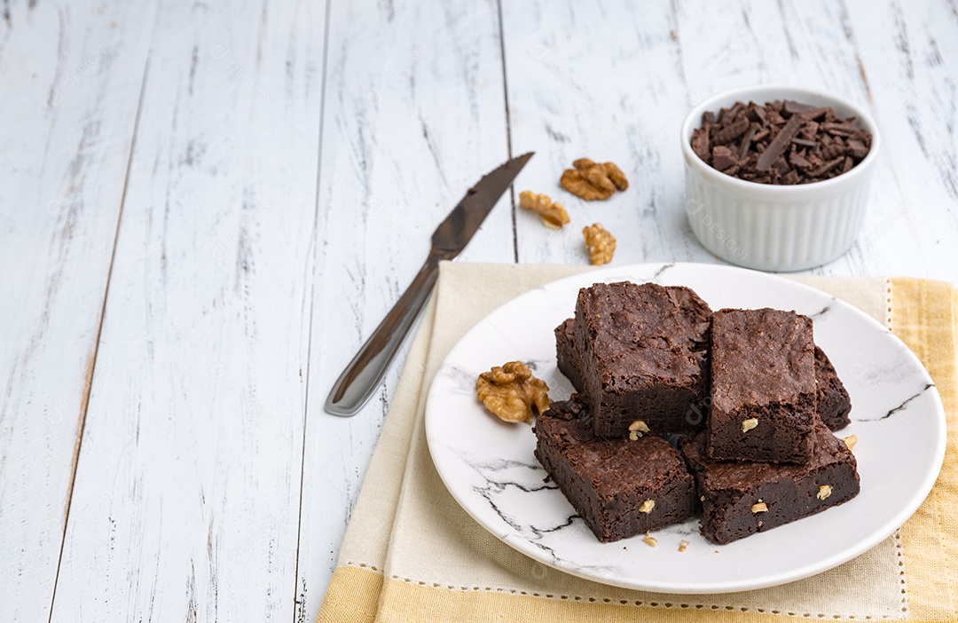 Brownies em um prato com pedaços de chocolate e nozes sobre mesa de madeira branca com espaço de cópia.