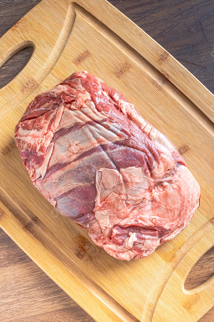 Bife do lombo cru inteiro em uma tábua de madeira, sobre uma mesa de madeira.