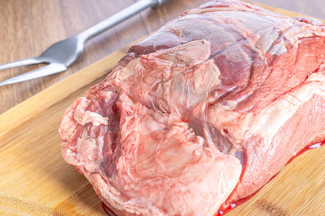 Bife do lombo cru inteiro em uma tábua de madeira, sobre uma mesa de madeira.