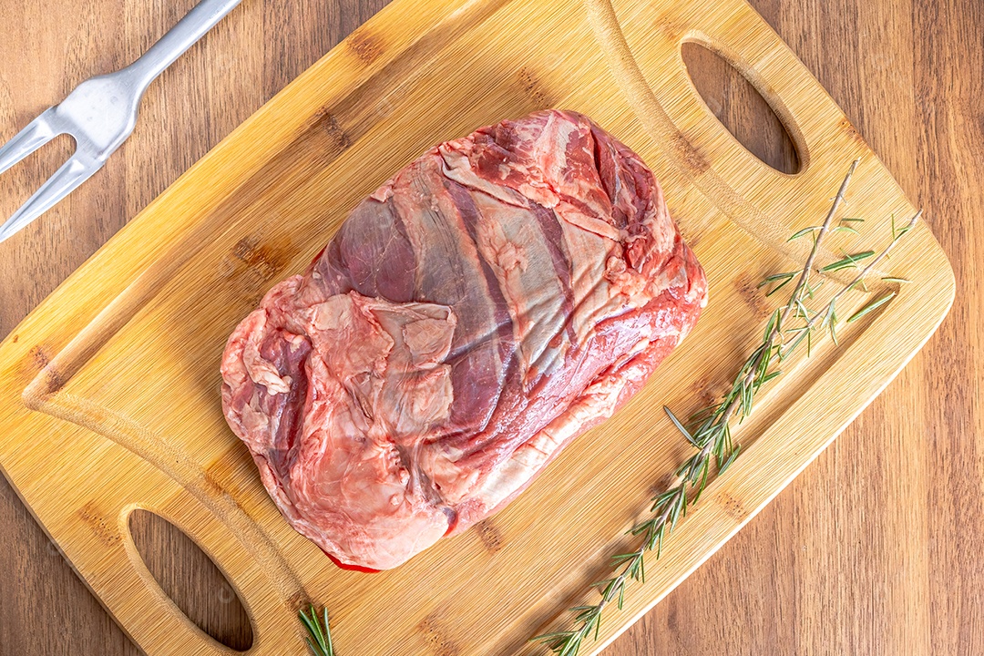 Bife do lombo cru inteiro em uma tábua de madeira, sobre uma mesa de madeira.