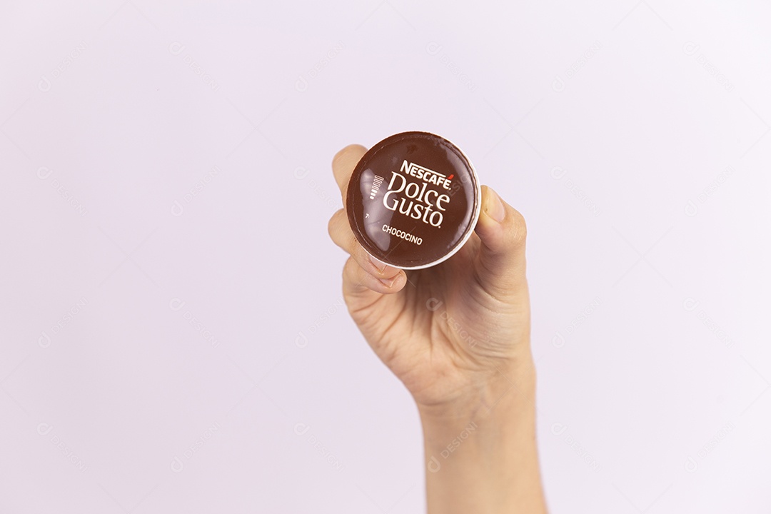 Mãos de pessoa segurando xícara e capsula de café