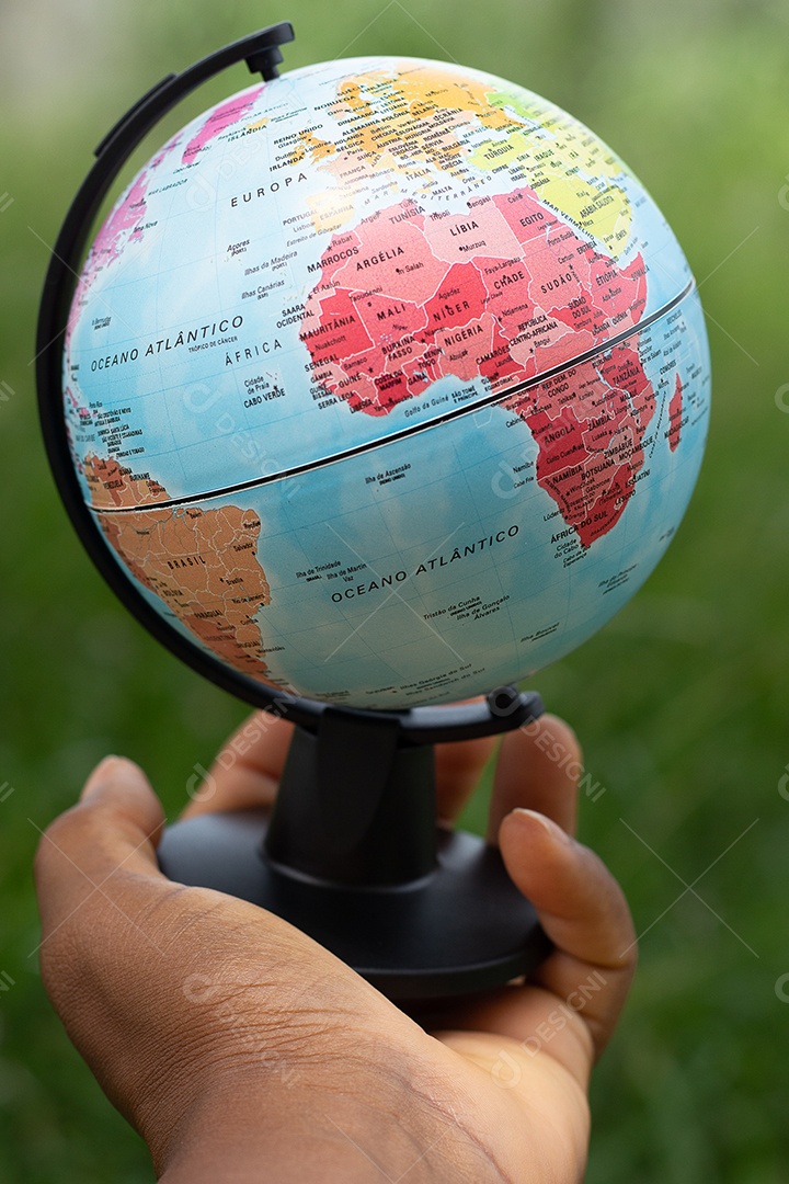 Mão segurando um globo terrestre com fundo verde mostrando a América do Norte e do Sul