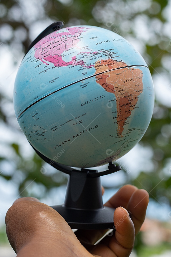 Mão segurando um globo terrestre com fundo verde mostrando a América do Norte e do Sul