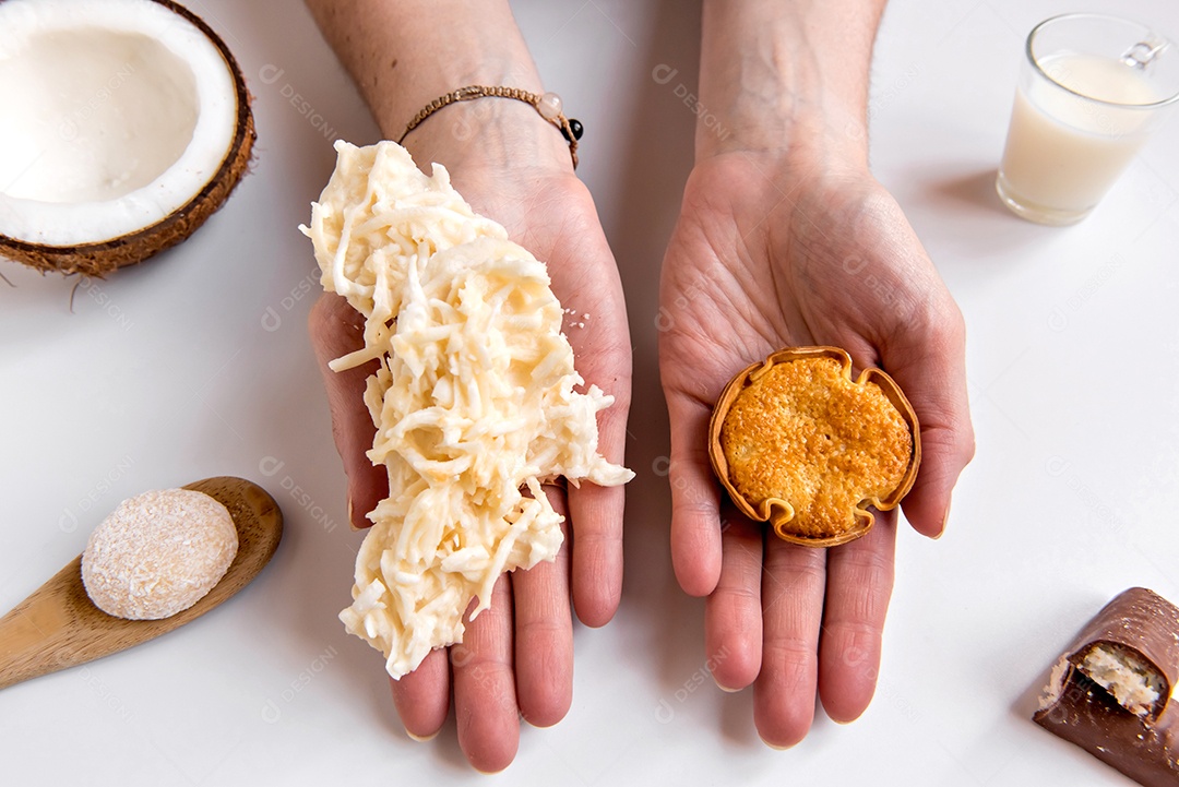 Mãos segurando coco e doce de coco (cocada) em fundo branco