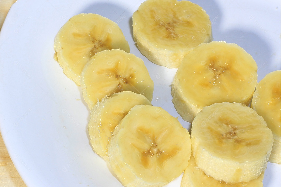 Fatias de banana em chapa branca sobre fundo de madeira. Lanche natural saudável.