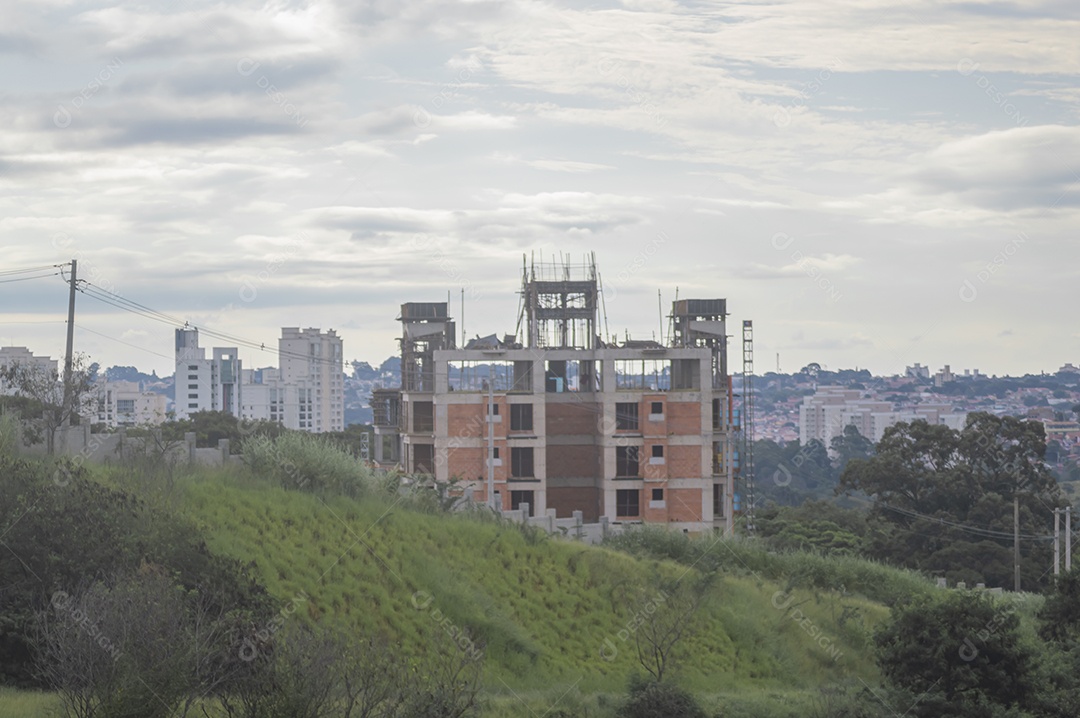 Construção em andamento com grama em volta da paisagem de uma cidade ao fundo.