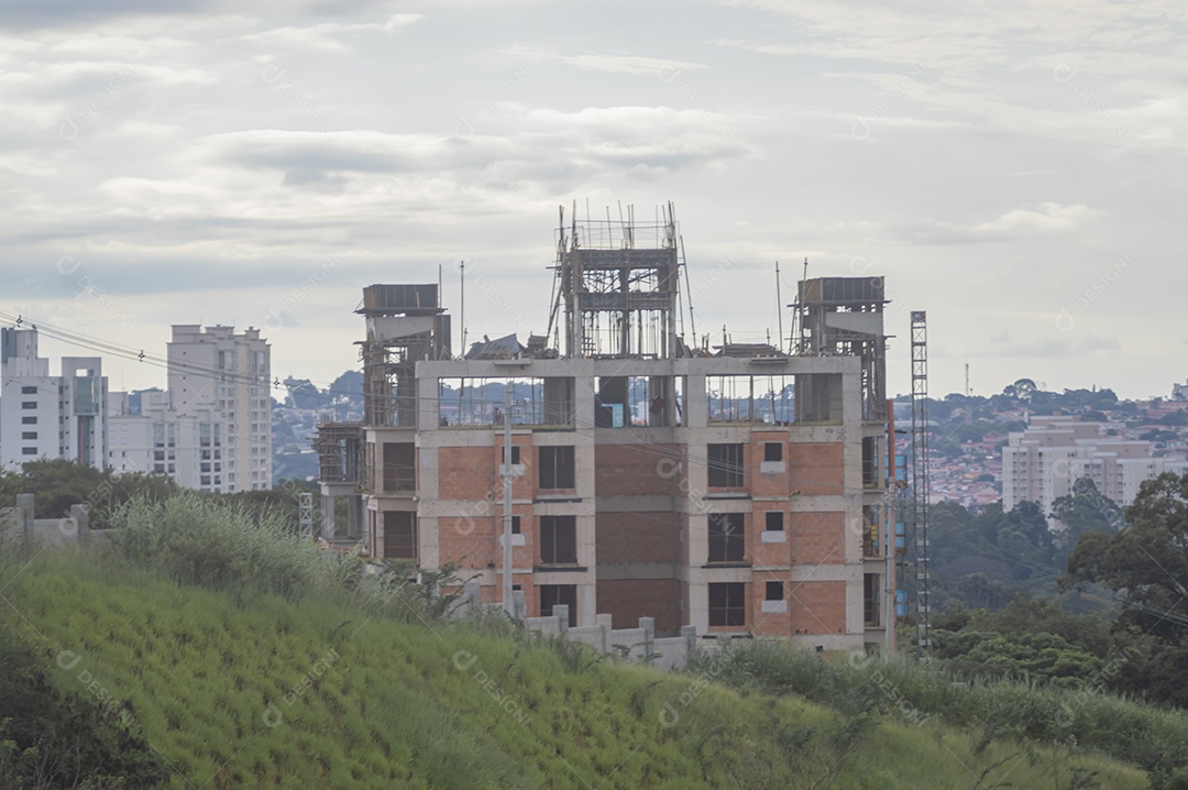 Construção em andamento com grama em volta da paisagem de uma cidade ao fundo.
