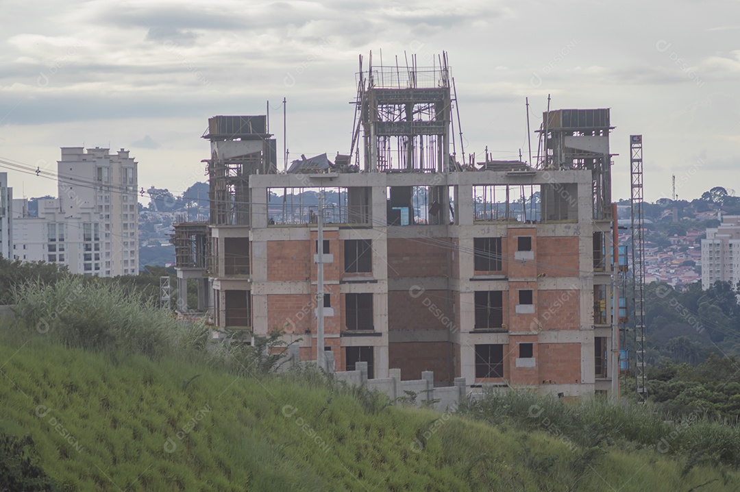 Construção em andamento com grama em volta da paisagem de uma cidade ao fundo.