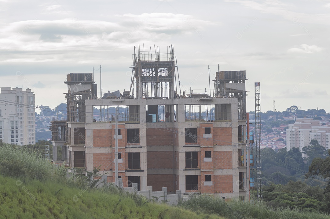 Construção em andamento com grama em volta da paisagem de uma cidade ao fundo.
