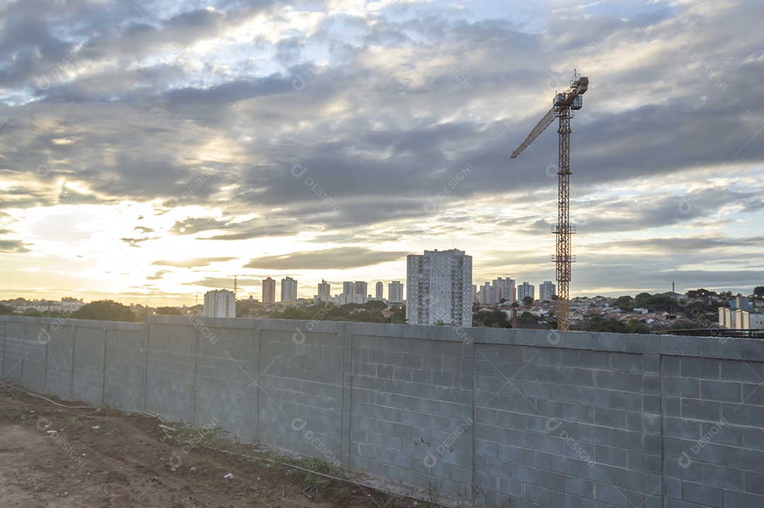 Guindaste gigante em uma obra em andamento com a cidade ao fundo em um final de tarde.