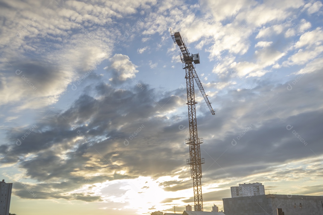 Guindaste gigante em uma obra em andamento com a cidade ao fundo em um final de tarde.