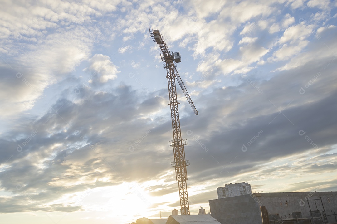 Guindaste gigante em uma obra em andamento com a cidade ao fundo em um final de tarde.