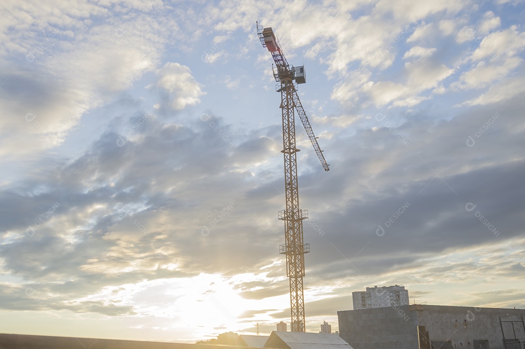 Guindaste gigante em uma obra em andamento com a cidade ao fundo em um final de tarde.