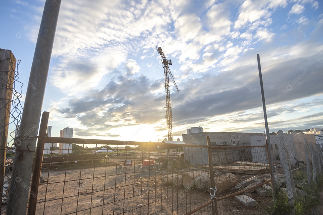 Guindaste gigante em uma obra em andamento com a cidade ao fundo em um final de tarde.