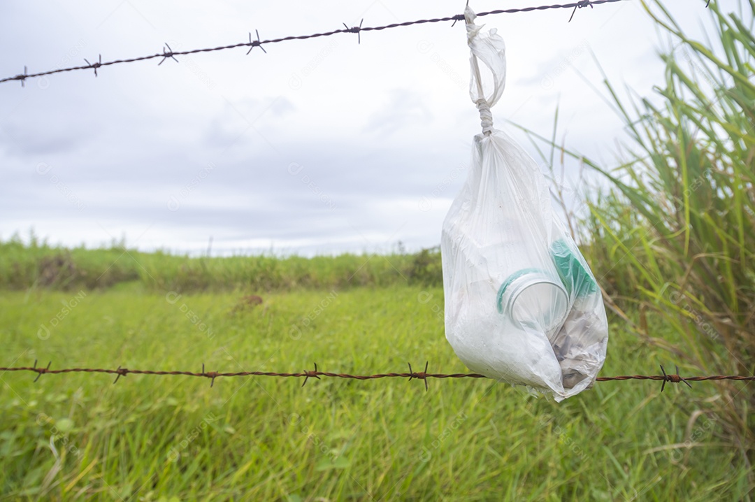 Saco com lixo amarrado em uma cerca com vegetação ao fundo em um dia nublado, conceito de poluição da natureza.