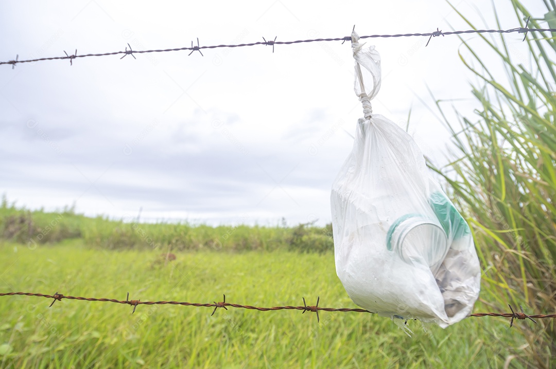 Saco com lixo amarrado em uma cerca com vegetação ao fundo em um dia nublado, conceito de poluição da natureza.