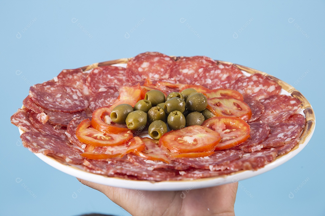 Mãos segurando prato de salame com azeitonas sobre fundo isolado