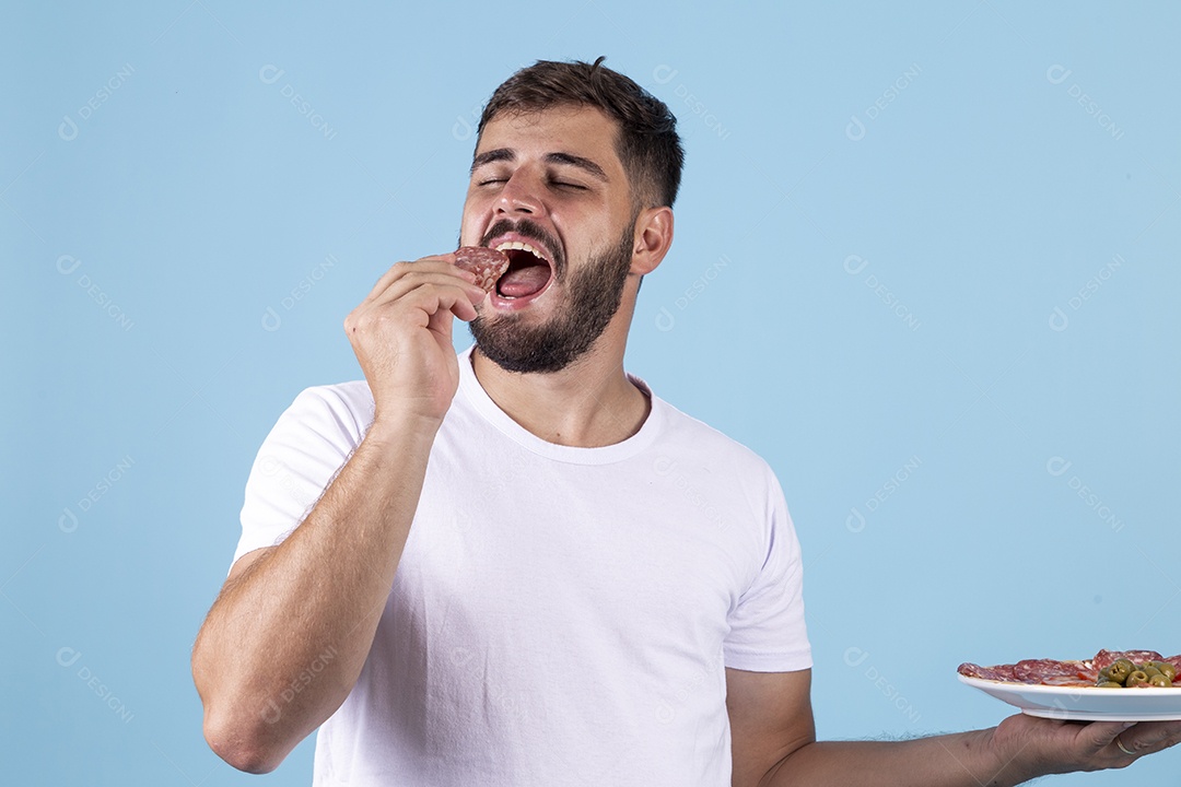 Homem jovem segurando prato de salame e se alimentando sobre fundo isolado