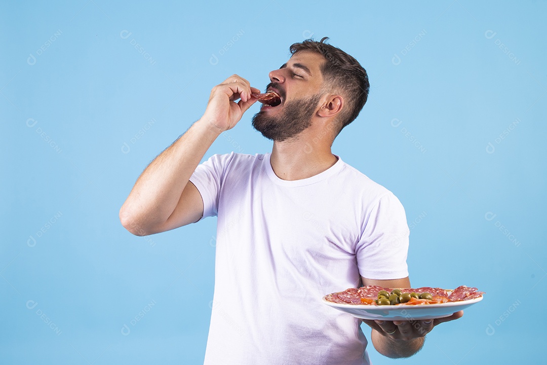 Homem jovem segurando prato de salame e se alimentando sobre fundo isolado