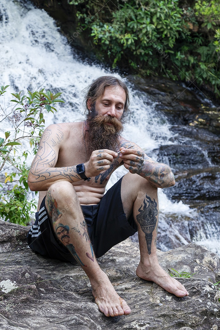 Homem barbudo fumando cannabis sobre cachoeira