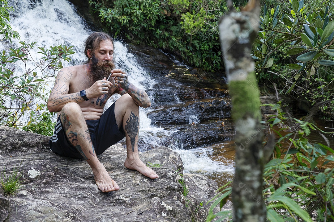 Homem barbudo fumando cannabis sobre cachoeira