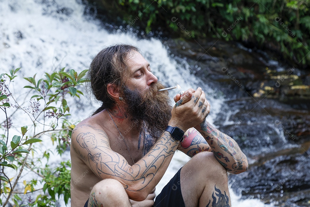 Homem barbudo fumando cannabis sobre cachoeira