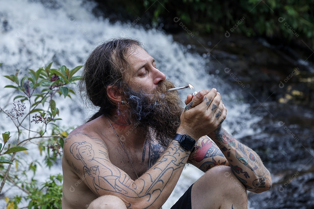 Homem barbudo fumando cannabis sobre cachoeira