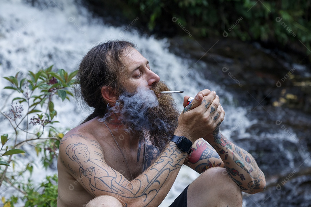 Homem barbudo fumando cannabis sobre cachoeira