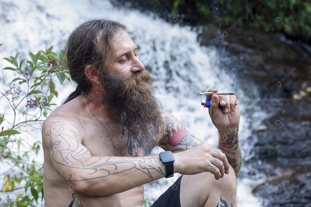 Homem barbudo fumando cannabis sobre cachoeira