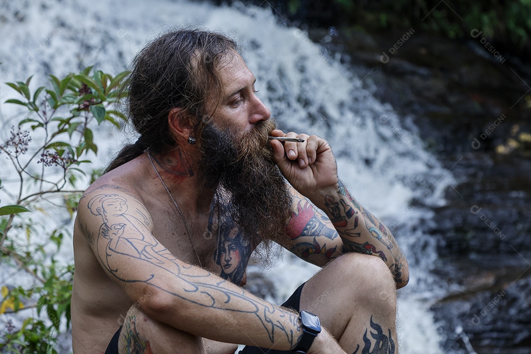 Homem barbudo fumando cannabis sobre cachoeira