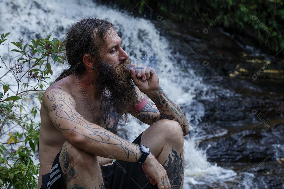 Homem barbudo fumando baseado sobre cachoeira