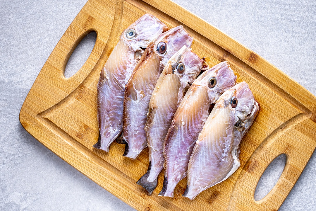 Peixe peroa limpo na tábua de madeira e coentros, pronto a fritar.