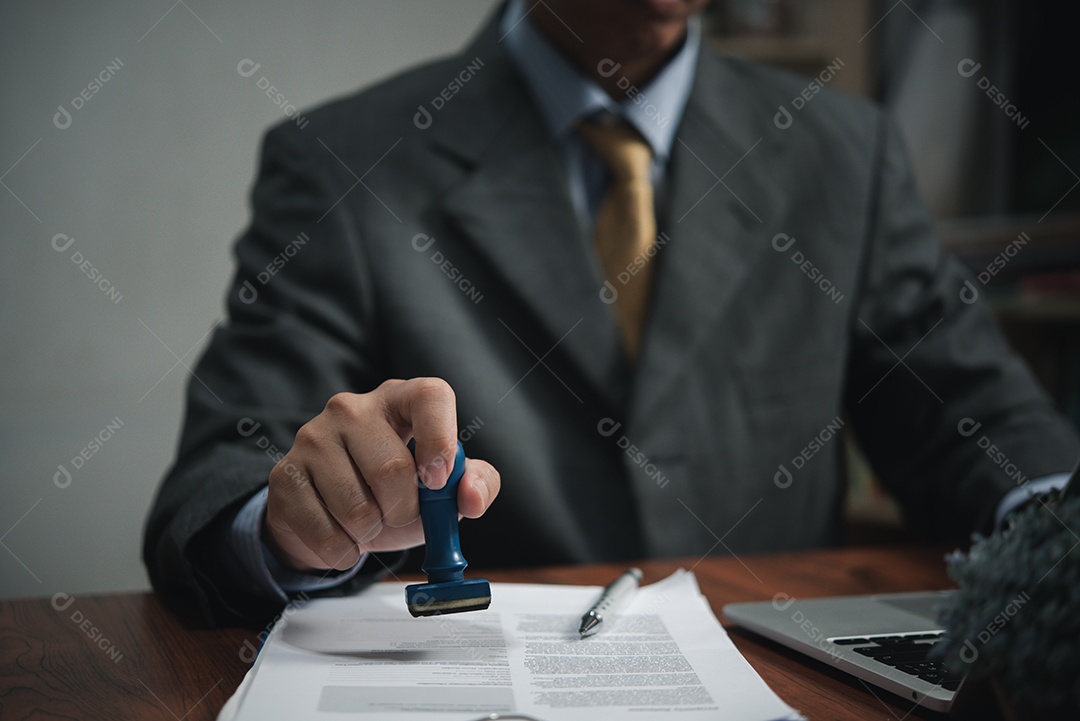 Mão de homem carimbando aprovação assinando contrato de documento ou papelada na mesa.