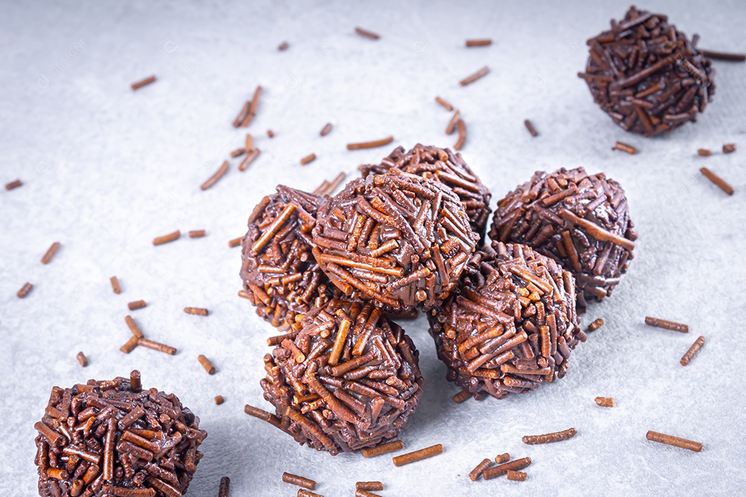 Vários doces brigadeiro em uma mesa branca com chocolates granulados