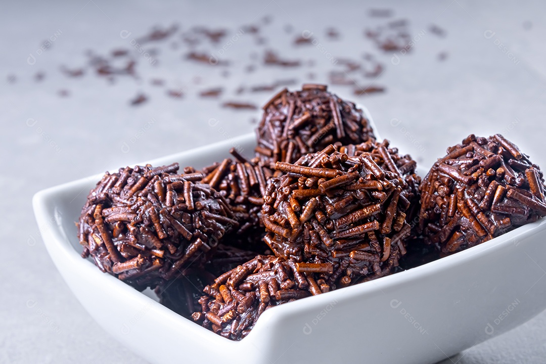 Vários bombons de brigadeiro em uma tigela branca com chocolate granulado sobre a mesa.