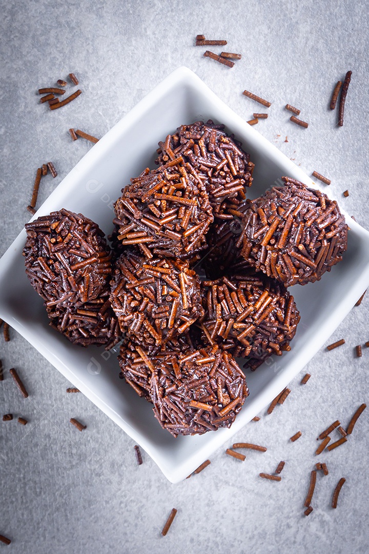 Vários bombons de brigadeiro em uma tigela branca com chocolate granulado sobre a mesa.