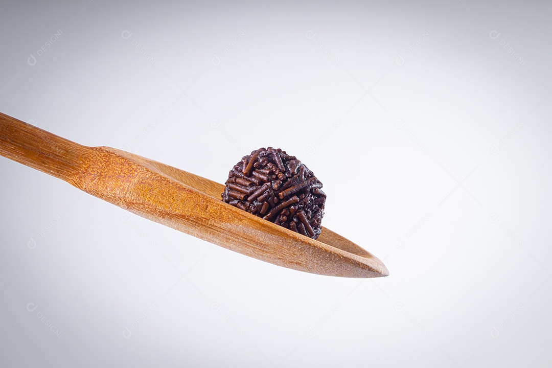Brigadeiro sendo feito na colher de pau com vários brigadeiros em uma tigela branca com chocolate granulado