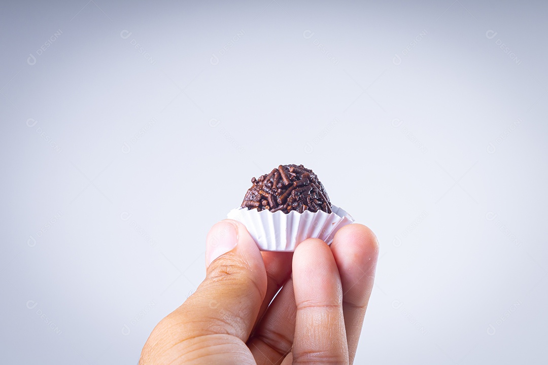 Brigadeiro em forma branca sendo oferecido com a ponta dos dedos sobre fundo branco.