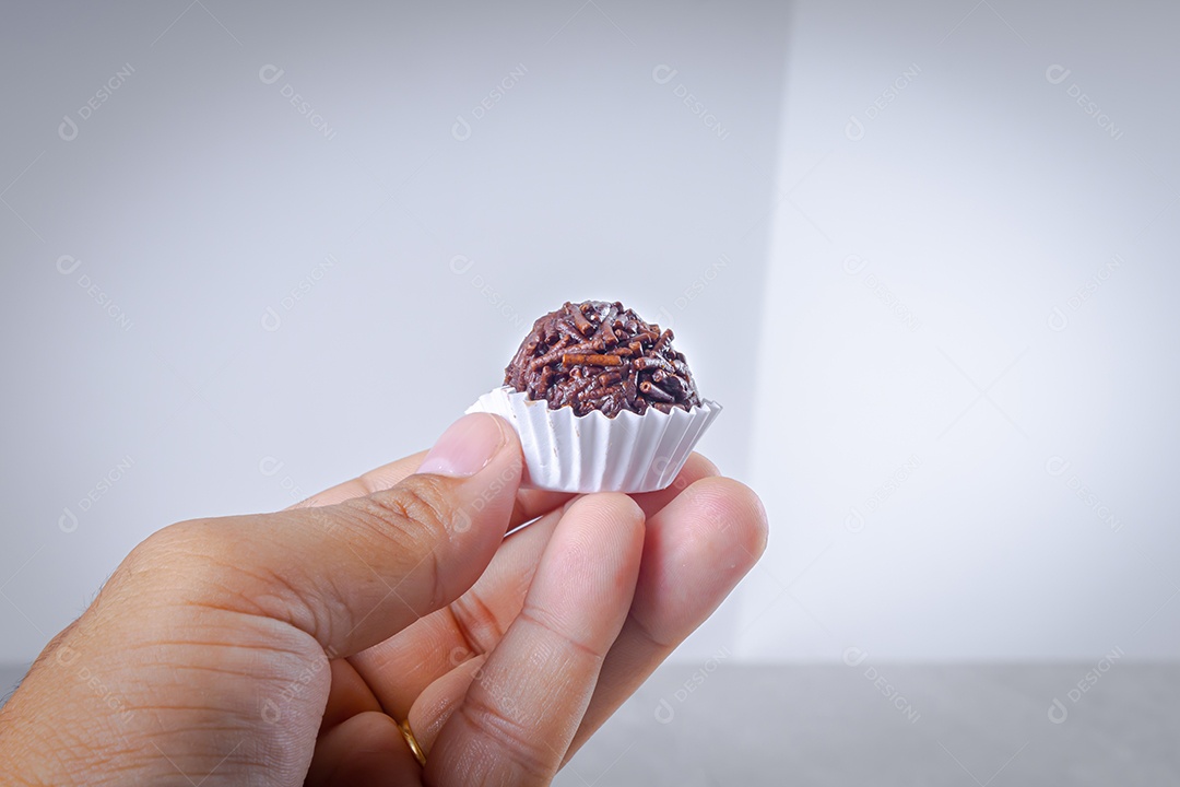 Brigadeiro em forma branca sendo oferecido com a ponta dos dedos sobre fundo branco.