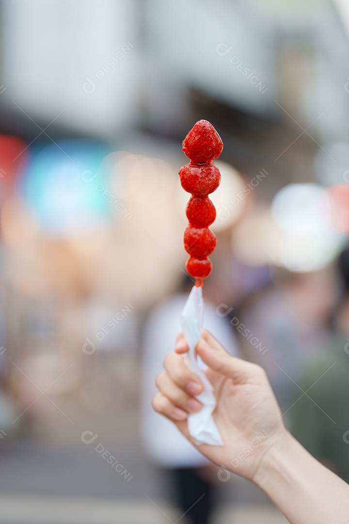 Mão de mulher segurando espeto de morango revestido de caramelo