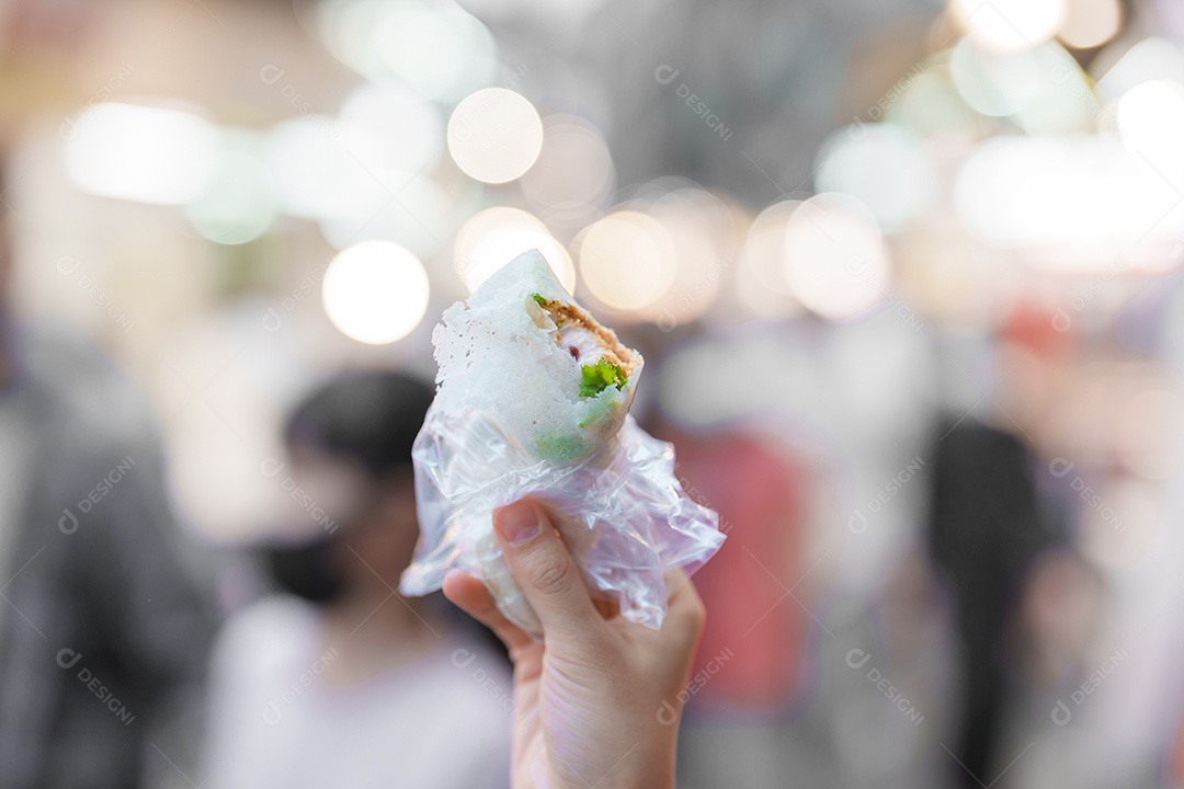 Mão de uma mulher segurando o rolo de sorvete de amendoim no mercado noturno.