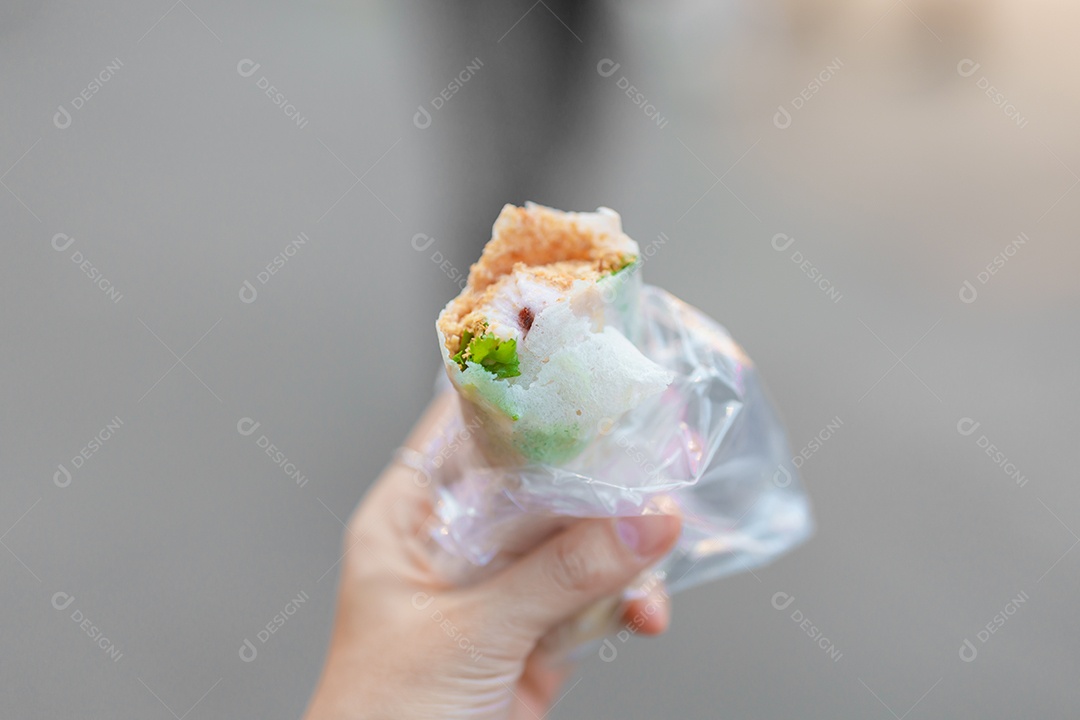 Mão de uma mulher segurando o rolo de sorvete de amendoim no mercado noturno.