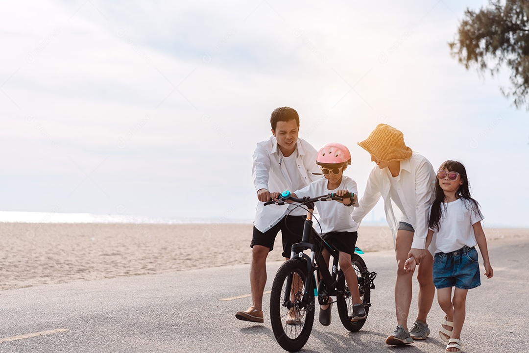 Família passeando pela praia ensinando filho a andar de bicicleta