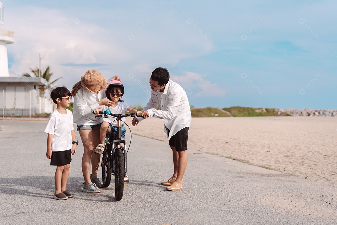 Família passeando pela praia ensinando filho a andar de bicicleta