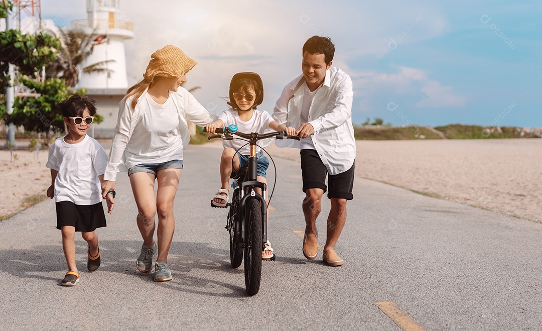 Família passeando pela praia ensinando filho a andar de bicicleta